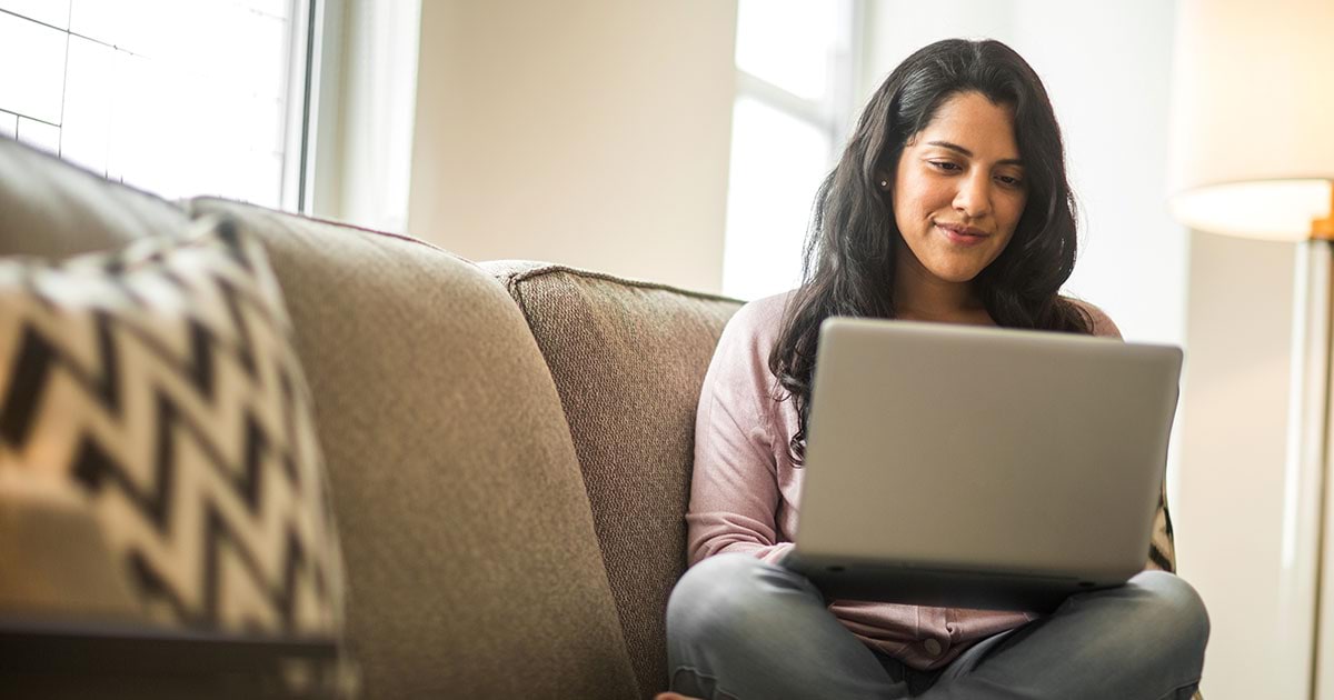 A smiling woman uses her laptop on the sofa